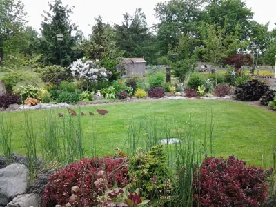 Green grass is surrounded by borders with lush plants and flowers