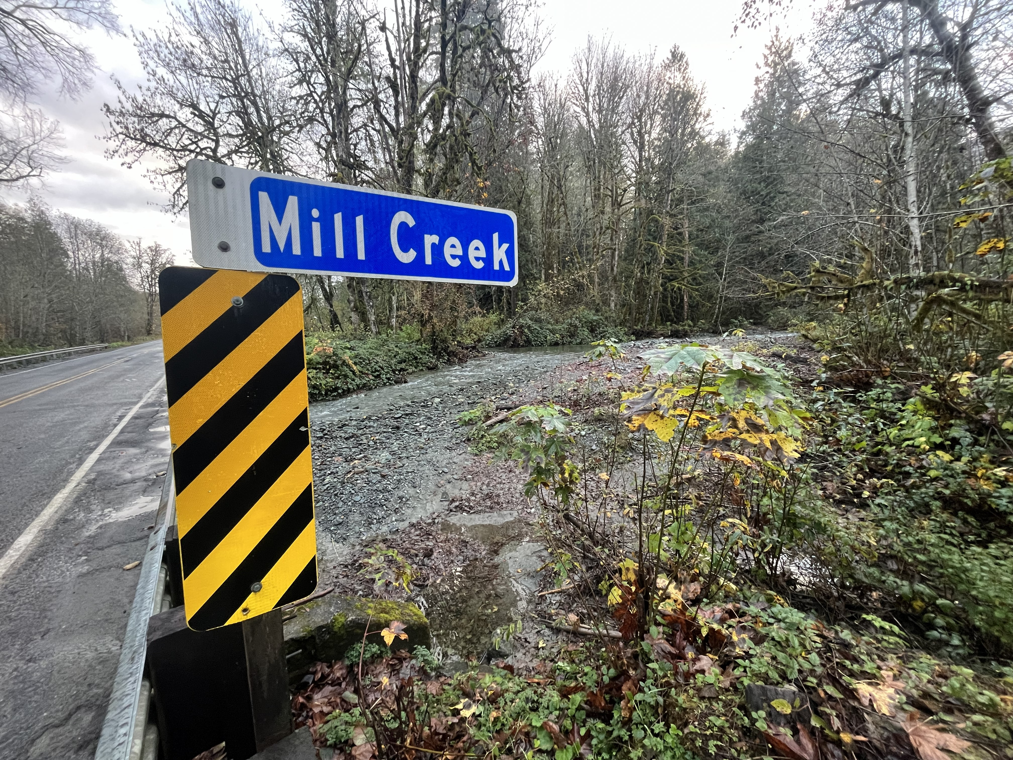 A road sign reading "Mill Creek" on a bridge crossing a creek with high water.
