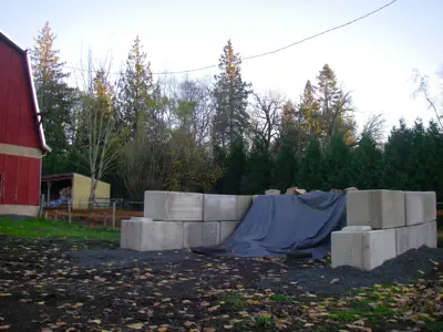 A large manure storage bin with large concrete blocks for walls, no floor or roof, but a tarp covering the manure.