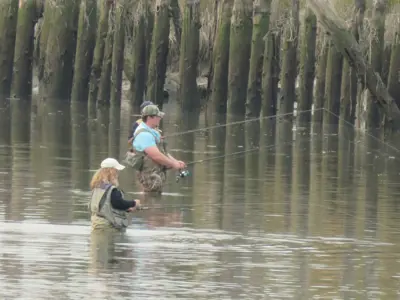 Three people wear waders while standing in the river fishing