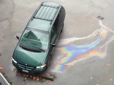 An oil sheen is flowing into a nearby storm drain from a parked van
